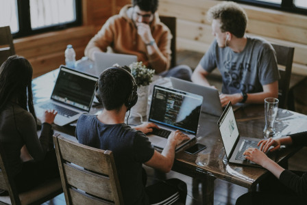 The photo presents a group of people working on laptops together.