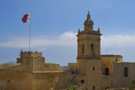 The photo presents the Maltese flag above historic buildings.
