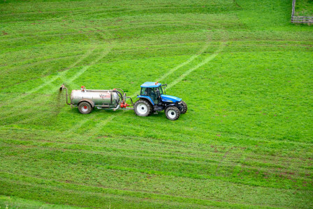 The photo presents a tractor working in a green field.