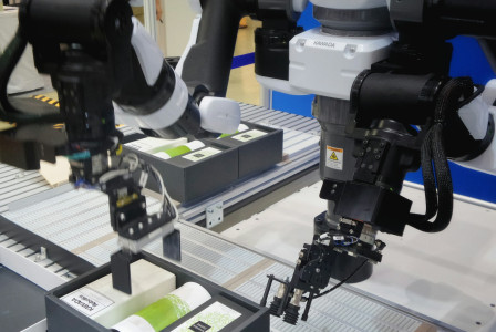 The photo presents robotic arms handling and packaging products on an automated production line.