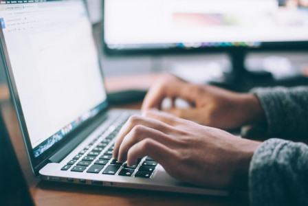 The photo presents a person typing on a laptop.