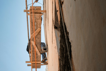 The picture presents a worker on a suspended scaffold beside a tall building wall.