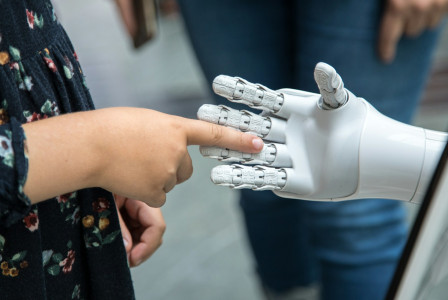 The photo presents a person interacting with a robotic hand.