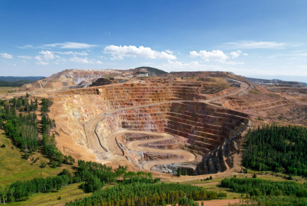 The photo presents a large open-pit mine surrounded by forest.