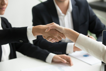 The photo presents two people shaking hands in a business meeting.