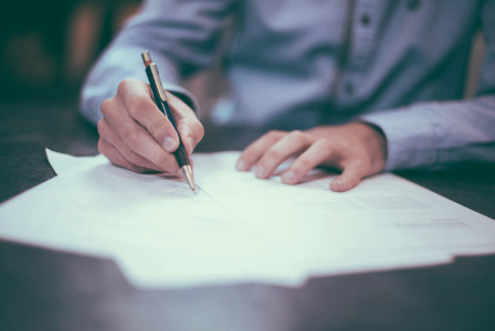 The photo presents a person signing a document.