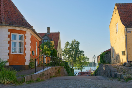 The photo presents a quiet street in Denmark with colourful historic houses leading toward the waterfront.