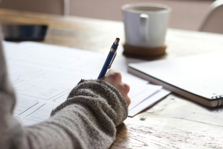 The photo presents a person writing notes at a desk.