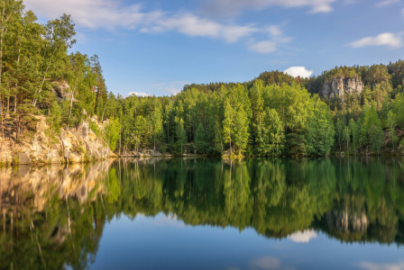 The photo presents a calm lake surrounded by a green forest.