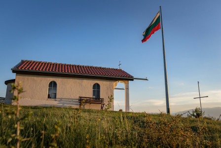 The photo presents the Bulgarian flag beside a small church.