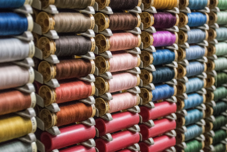 Rows of sewing thread spools arranged by colour, including shades of pink, blue, green, purple, grey and yellow.
