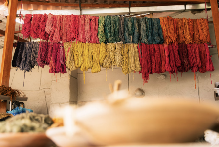 Rows of yarn hanging to dry in a textile workshop, arranged by colour in shades of red, pink, green, blue, orange, yellow and grey.