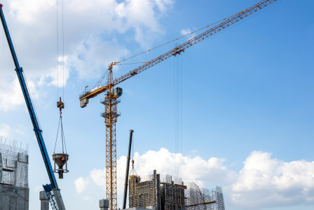 The picture describes a large-scale construction site where tower cranes and lifting equipment are being used to build a reinforced concrete structure.