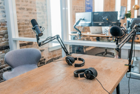 The photo presents a podcast recording setup with two microphones on adjustable arms and two pairs of headphones on a wooden table.