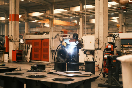 The photo presents a worker welding metal in a factory.