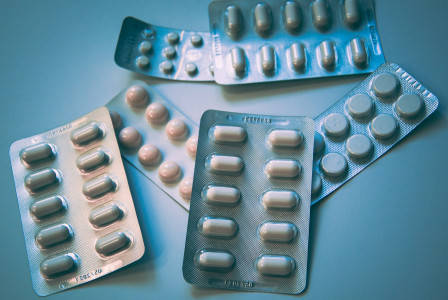 The photo presents several blister packs of assorted tablets and capsules arranged on a blue surface.