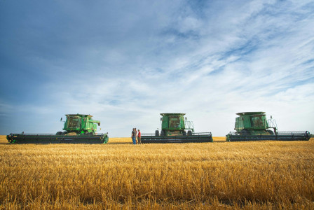 The photo presents a tractor pulling a baler through a harvested field dotted with straw bales under a blue sky.