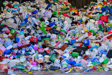 The photo presents a large pile of discarded plastic bottles, buckets, food tubs and other household containers in various colours.