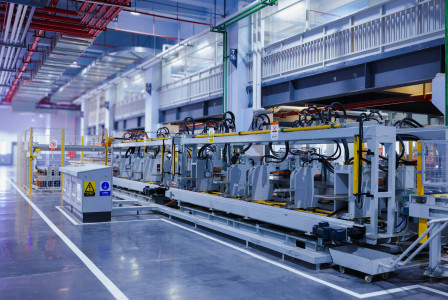 The photo presents an automated factory production line with rows of machinery, a control cabinet and yellow safety barriers.