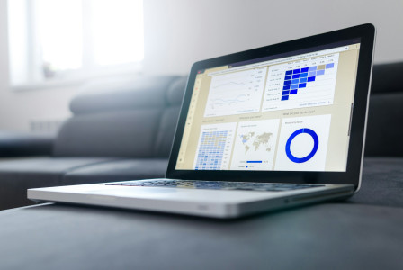 The photo presents a laptop displaying web analytics dashboards with charts, a user-retention cohort grid, a world map and a device breakdown.