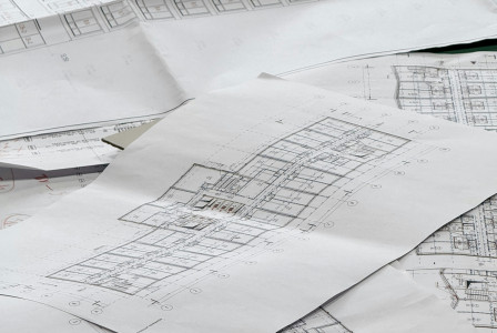 The picture shows several large architectural and engineering floor plans spread across a table