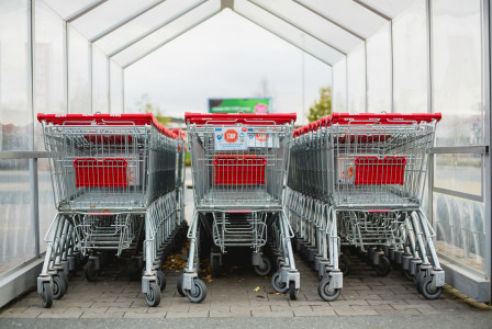 The photo presents three rows of nested metal shopping trolleys with red handles inside a covered shelter.