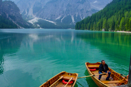 Photo presenting two wooden rowboats floating on a turquoise mountain lake, surrounded by forested slopes and mist-covered peaks.