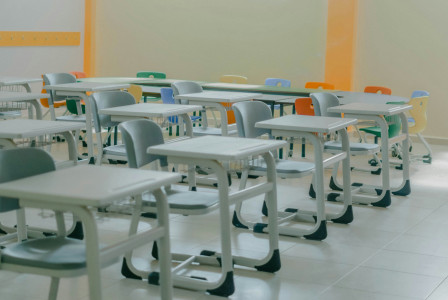 The picture shows an empty classroom with rows of desks and colorful chairs, representing educational infrastructure and modern learning environments.