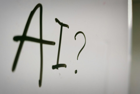 The photo presents the letters “AI” followed by a question mark, handwritten in black marker on a whiteboard.