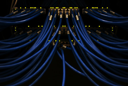 The photo presents blue Ethernet cables connected to network switches, with glowing indicator lights in a dark equipment rack.