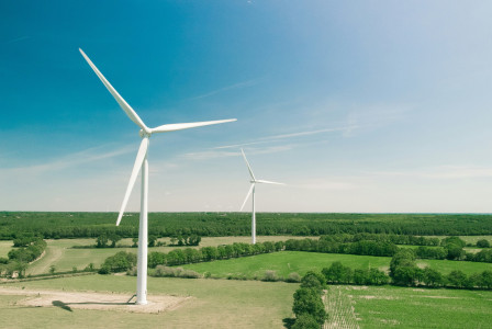 The picture describes a wind farm with modern wind turbines generating renewable energy across a green rural landscape under a clear blue sky.