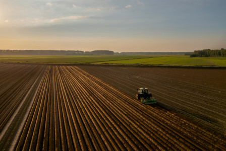 The photo presents a tractor working in a brown field.