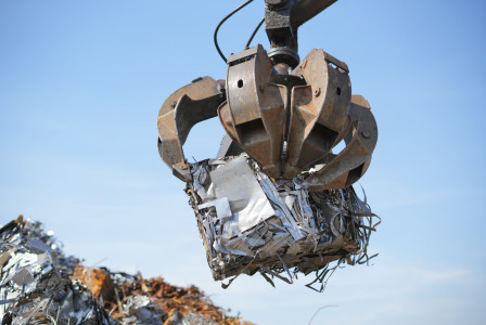 The photo presents a crane lifting compressed scrap metal.