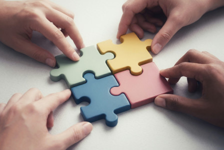 4 connected puzzle pieces in different colours and a hand holding each one