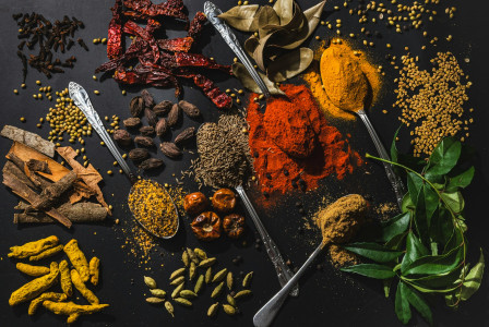 The photo presents a variety of spices, herbs, seeds, and dried ingredients arranged on a dark surface.