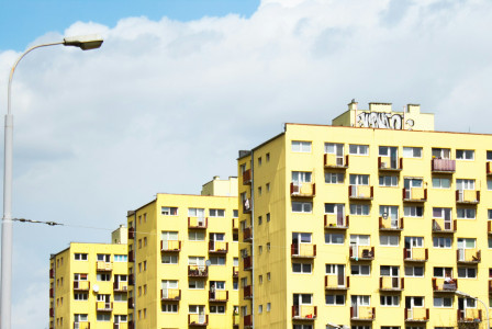The picture shows large yellow apartment blocks in Poland, with rows of windows and small balconies beneath a bright, cloudy sky.
