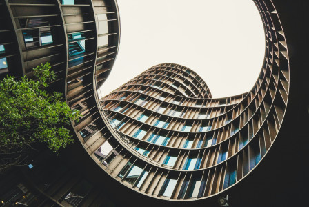 This picture captures a modern architectural courtyard viewed from below, looking upward toward the sky through the centre of a curved building.