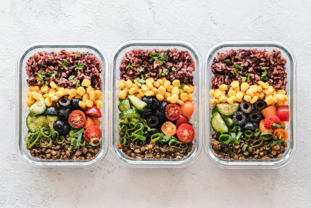The photo presents three meal-prep containers filled with rice, lentils, corn, olives, cucumber, tomatoes, and fresh herbs.