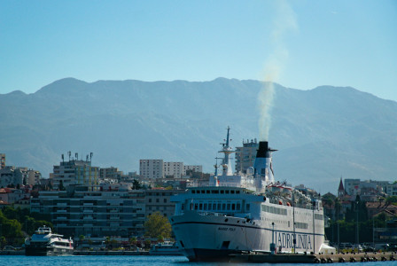 The photo presents a ferry in a coastal city with mountains in the background.