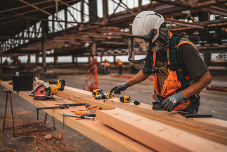 This picture shows a construction worker using tools to work on wooden beams at a construction site.