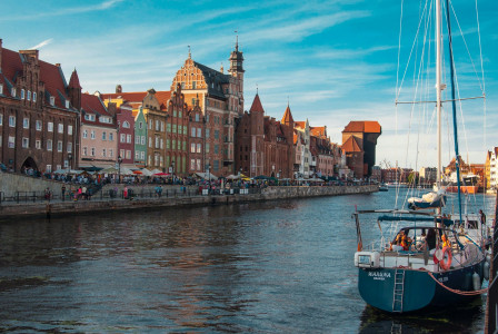 The photo presents the historic waterfront of Gdańsk, Poland, with the Motława River and the medieval Crane in the background.
