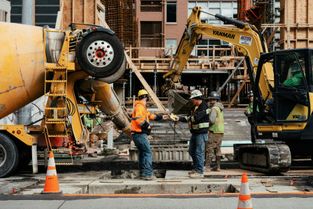This picture shows an active construction site where workers are coordinating around heavy machinery and concrete works during the structural phase of a building project.