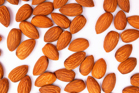 The photo presents whole almonds scattered across a white background.