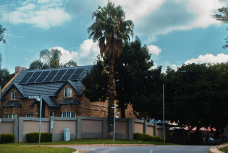 This picture shows a residential house with solar panels installed on the roof, surrounded by trees and greenery.