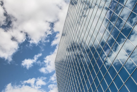 An illustrative photo of a modern building with reflective glass windows, capturing the sky and clouds in a stunning display