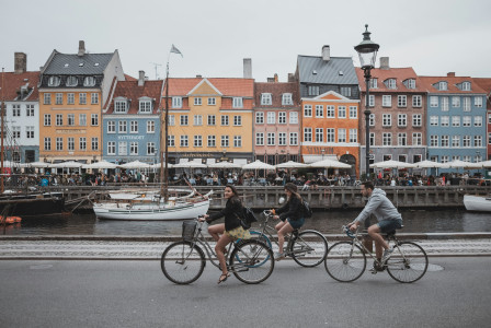 An illustrative photo of three people riding bicycles near a body of water and buildings