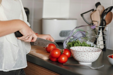 An illustrative photo of a woman cutting tomatoes in kitchen
