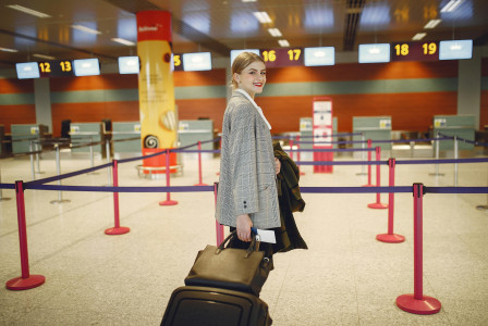 Photo by Pexels An illustrative photo of a cheerful female passenger walking with luggage to a departure check-in counter