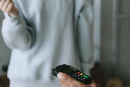 An illustrative photo of a person holding a phone with another person standing and holding a book in the background