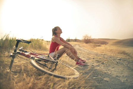 An illustrative photo of a sportive woman with a bicycle resting on a countryside road in sunlight